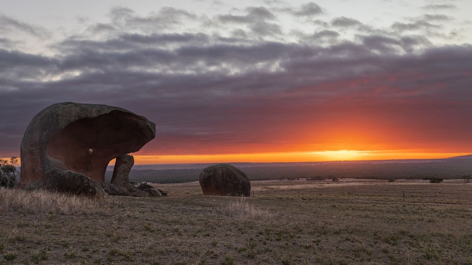 A sunset over a grassy field with large boulders.