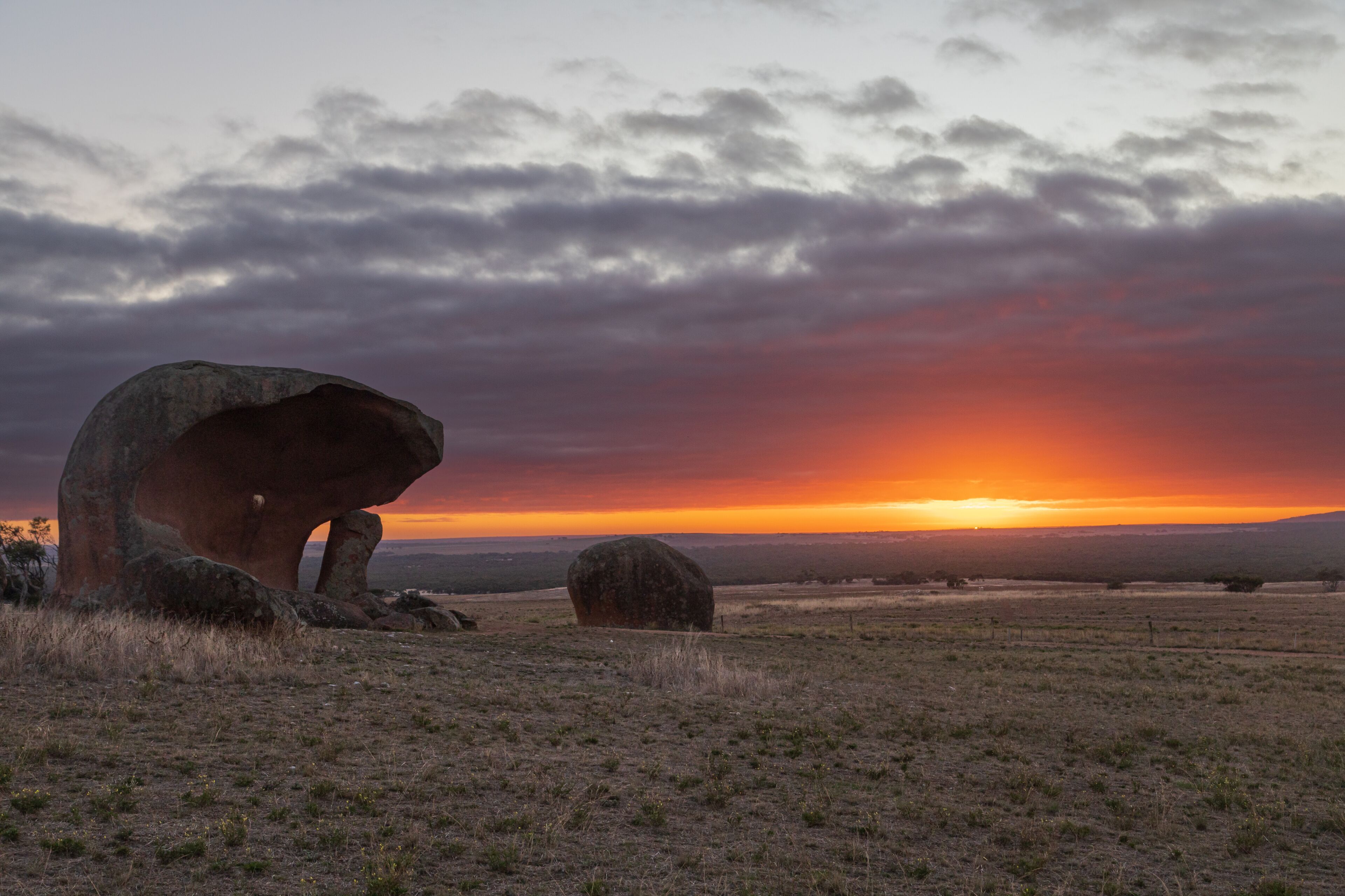 A sunset over a grassy field with large boulders.