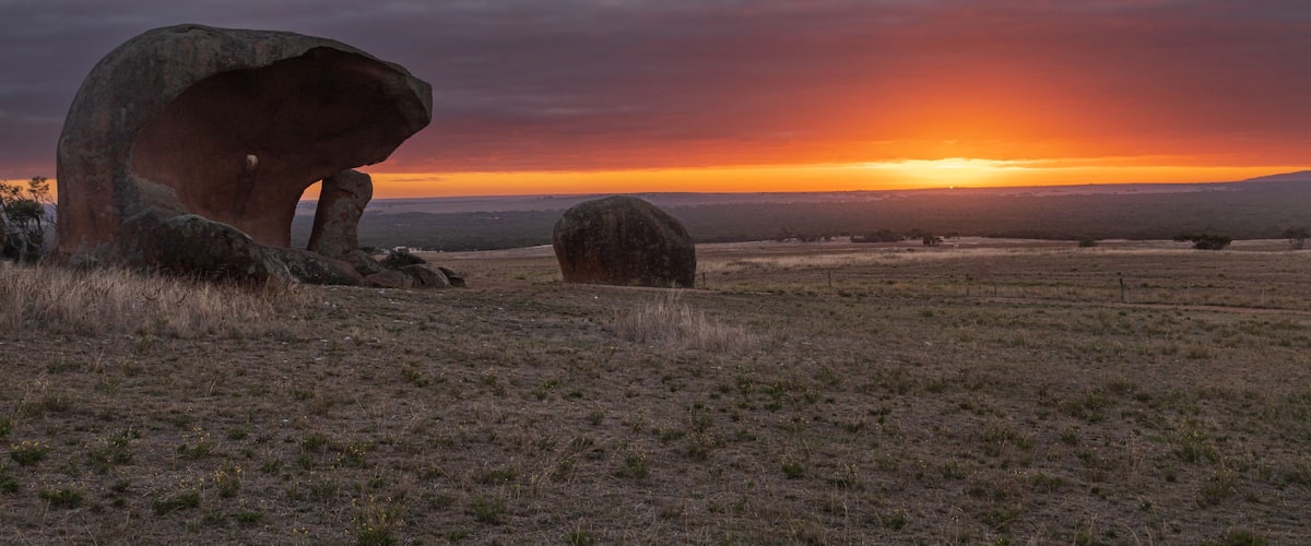 A sunset over a grassy field with large boulders.