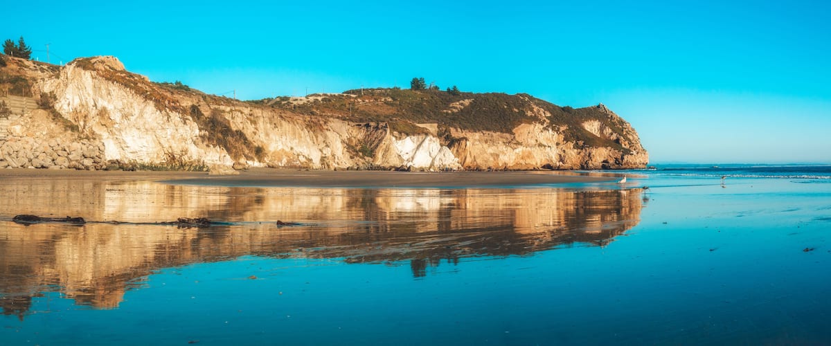 A coastal landscape with cliffs, a sandy beach, and a calm sea.