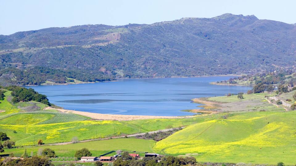 A lake surrounded by green hills and a few buildings.