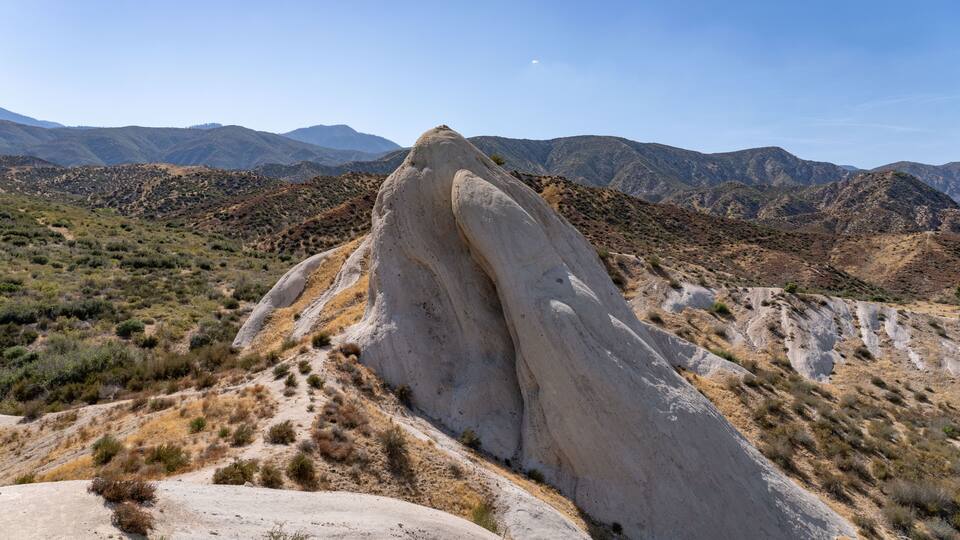 A large rock formation in a desert landscape with distant mountains.