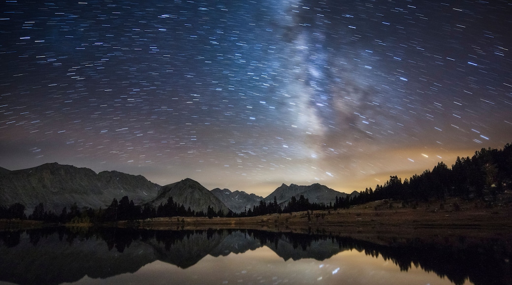 Sternenklarer Nachthimmel ĂŒber einem Gebirge, spiegelnd wider in einem ruhigen See.