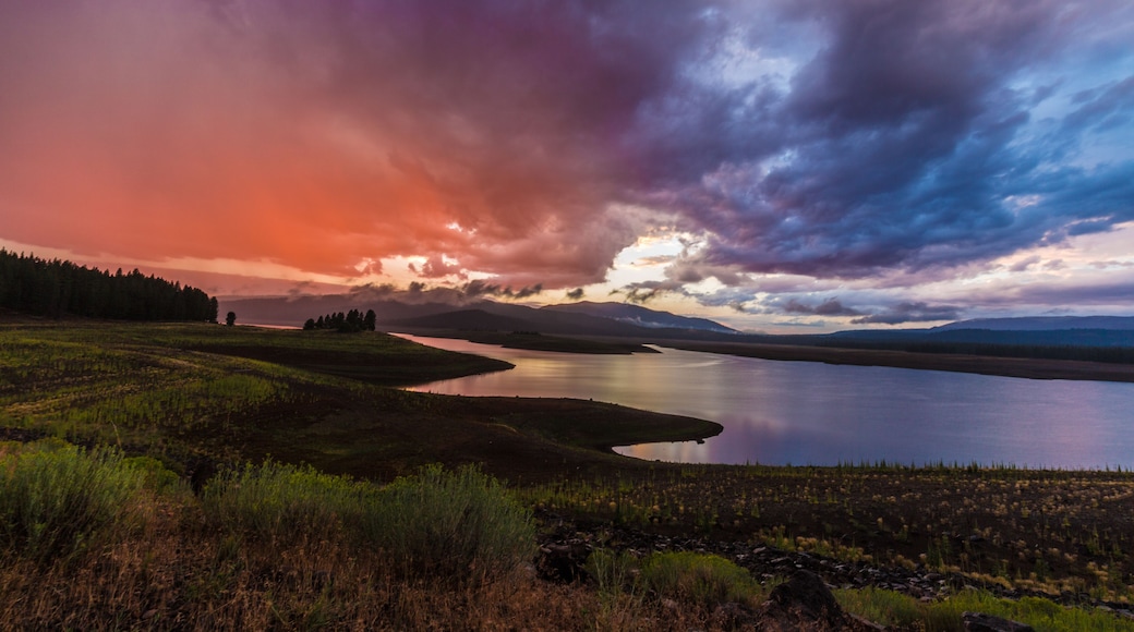 A lake surrounded by mountains and a forest at sunset.