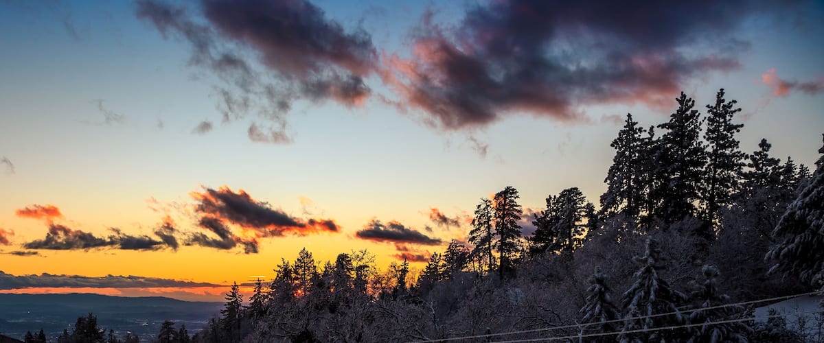 A sunset over a mountainous landscape with dense forests and a clear sky.