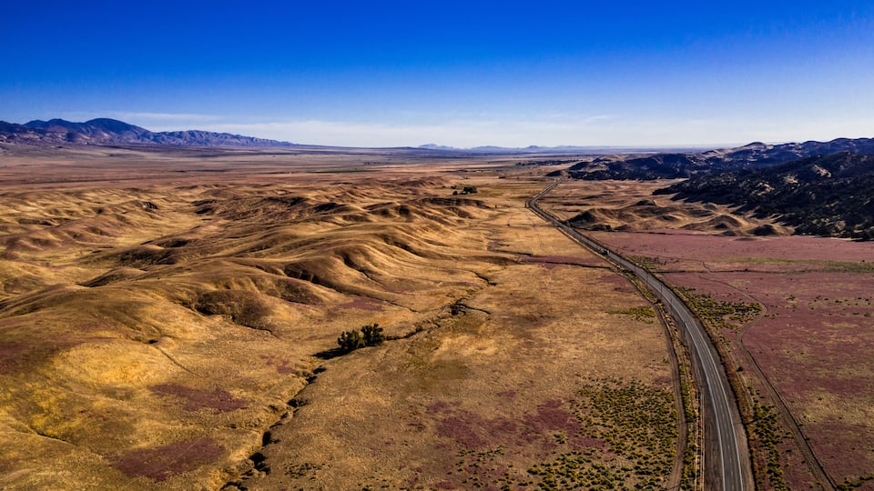 A vast, undulating landscape with a winding road cutting through it.
