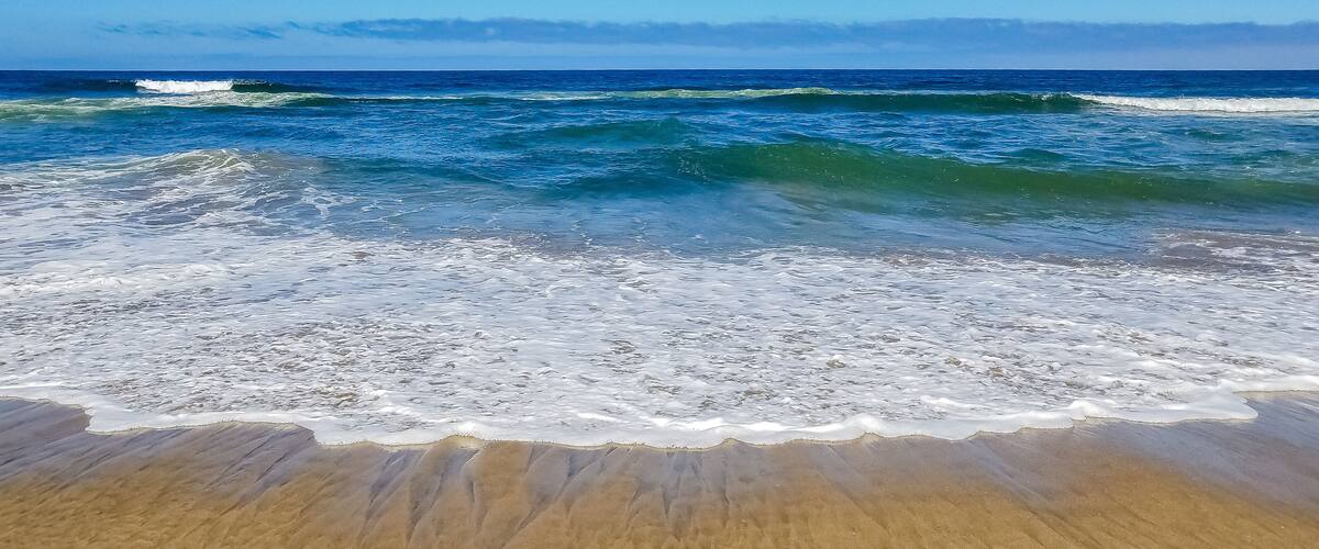 A beach with waves crashing onto the shore under a clear blue sky.
