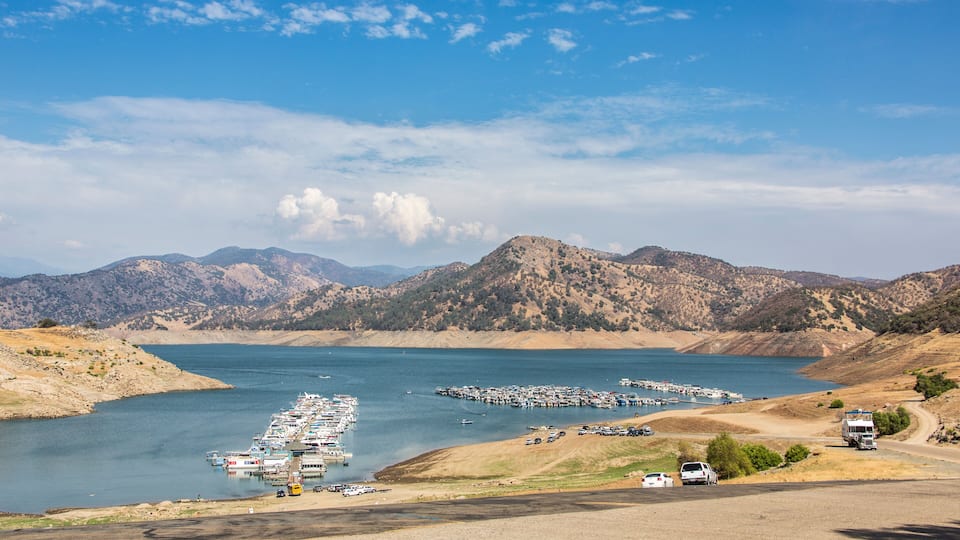 A marina with boats docked, a road with vehicles, and mountains in the background.