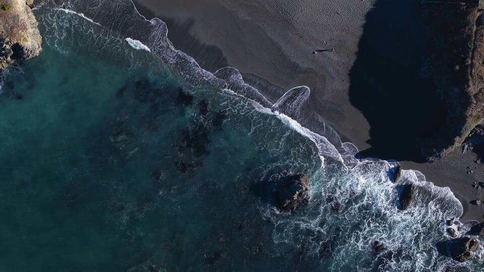 A coastal area with waves crashing onto a sandy beach and rocky outcrops.