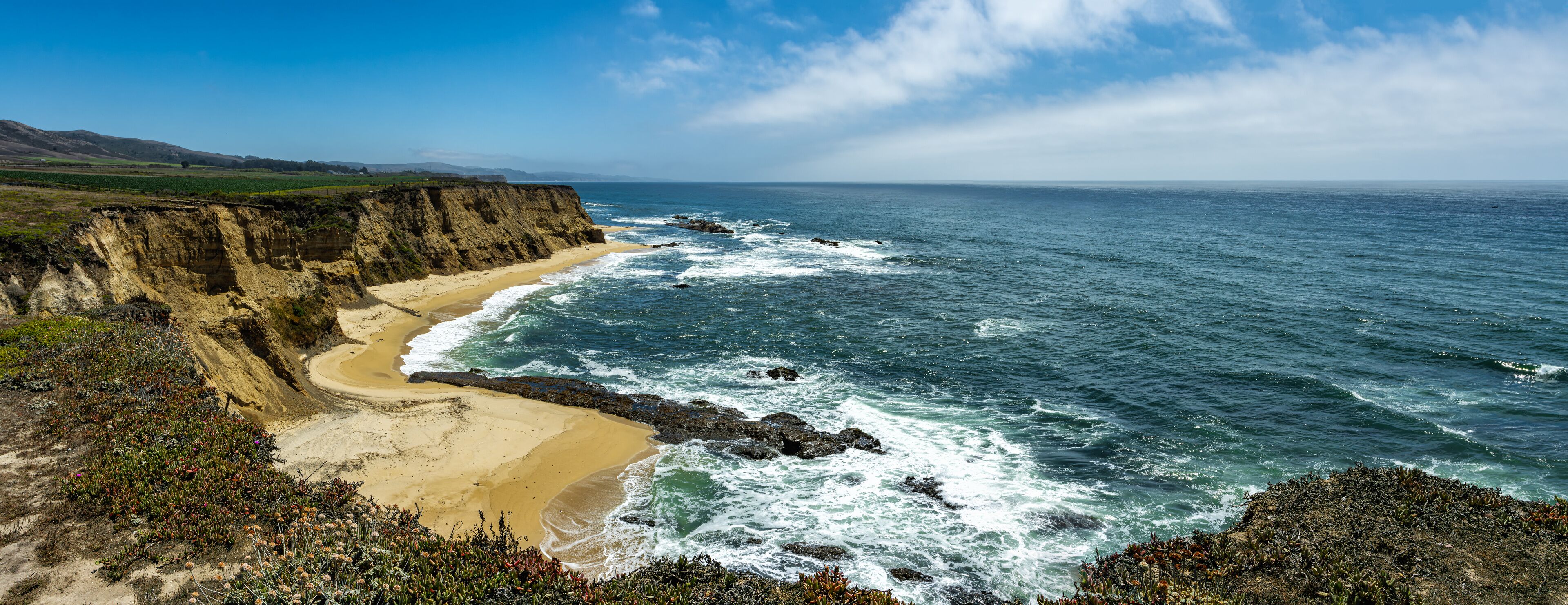 A coastal landscape with a sandy beach, rocky cliffs, and the ocean.