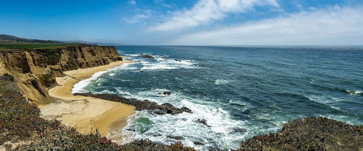 A coastal landscape with a sandy beach, rocky cliffs, and the ocean.