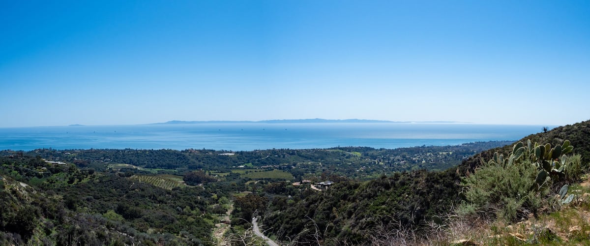 A coastal landscape with a clear view of the ocean, rolling hills, and a distant mountain range.