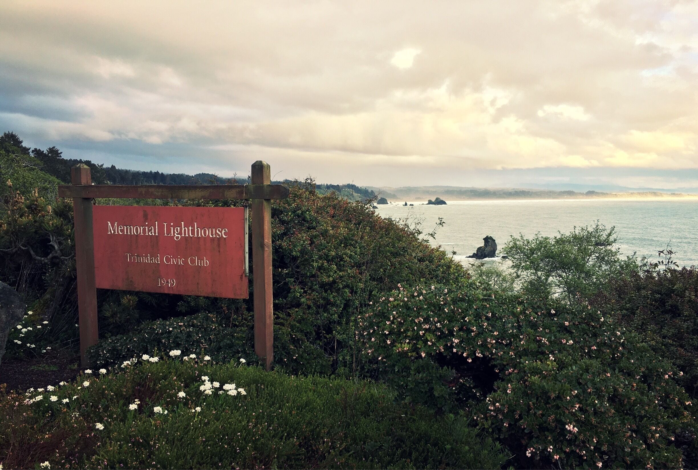A sign for Memorial Lighthouse, Trinidad Civic Club, 1949, with a view of the sea and distant islands.