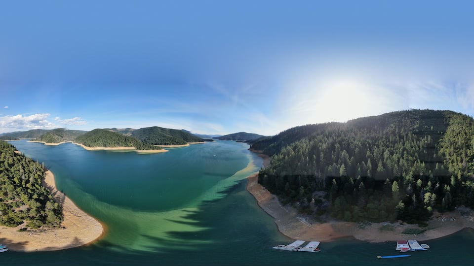 A coastal landscape with a clear blue sky, a large body of water, and a forested hill.