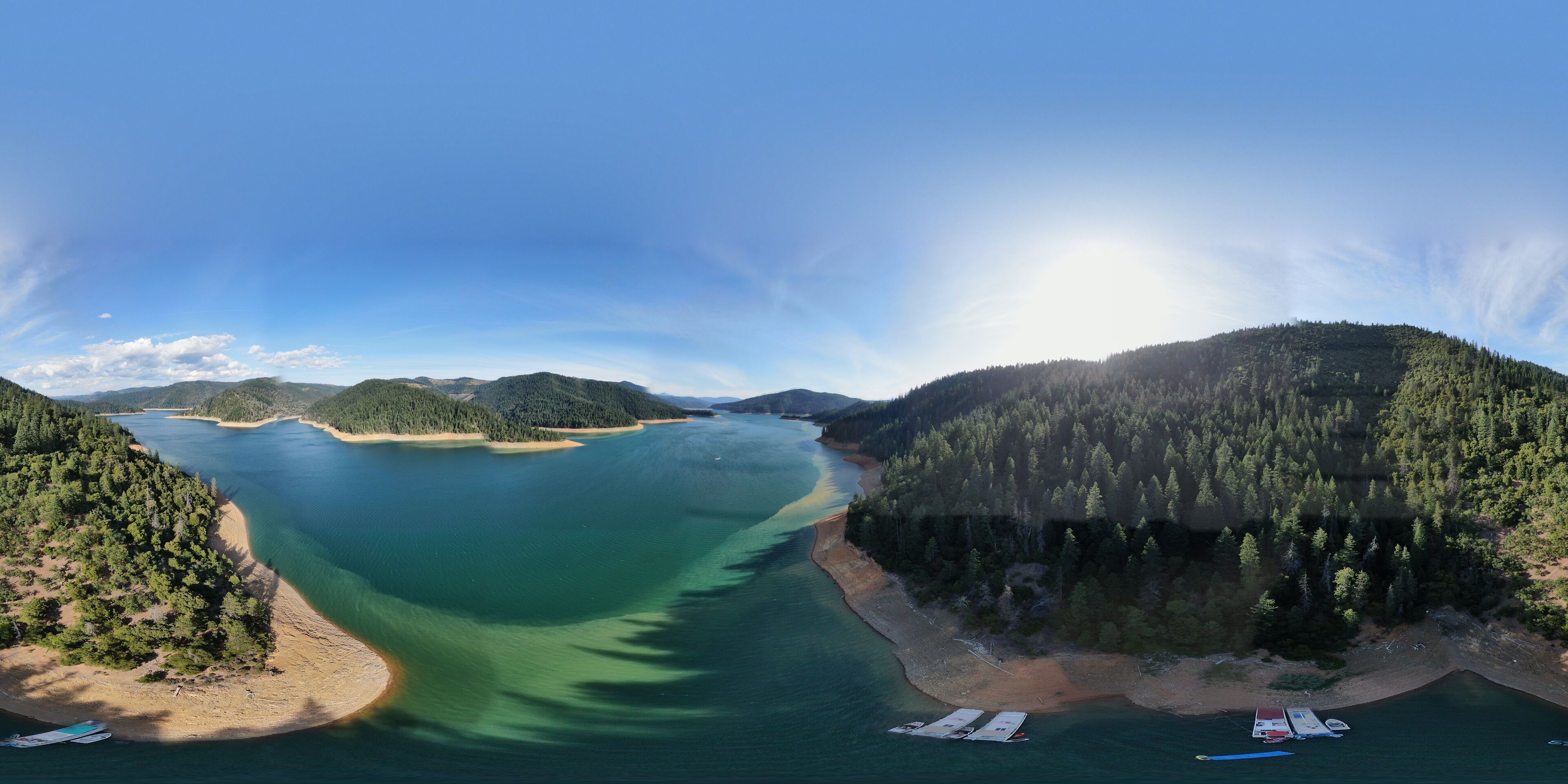 A coastal landscape with a clear blue sky, a large body of water, and a forested hill.