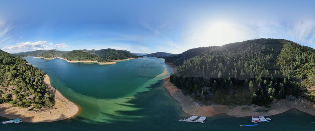 A coastal landscape with a clear blue sky, a large body of water, and a forested hill.