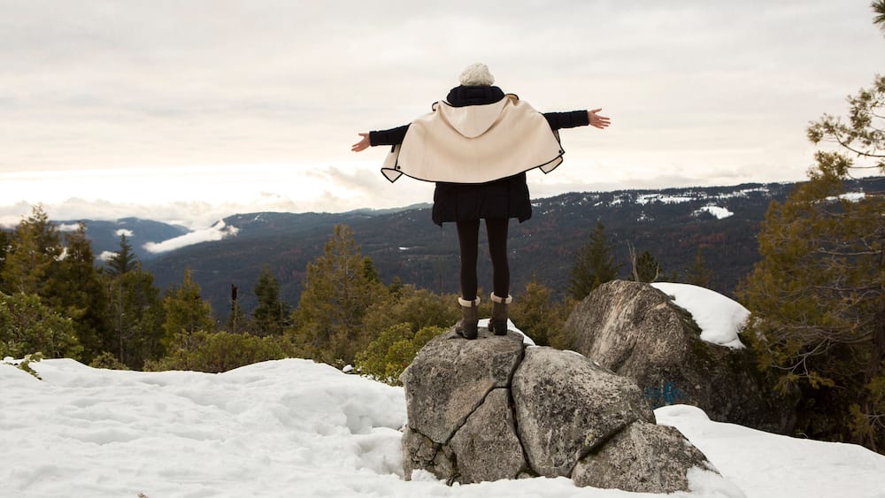 Young woman standing on rock on snow covered mountain, rear view, Twain Harte, California, USA
