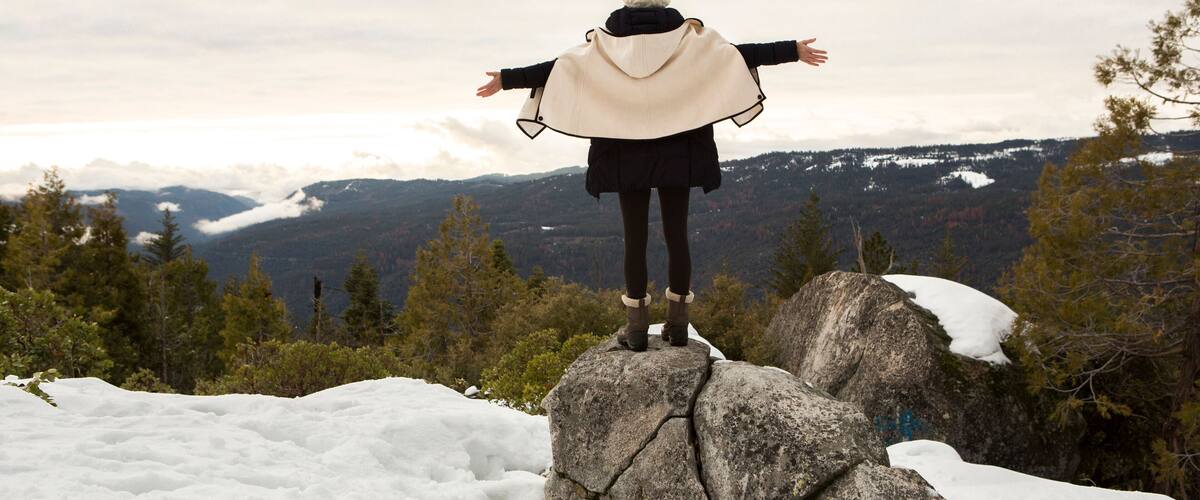 Young woman standing on rock on snow covered mountain, rear view, Twain Harte, California, USA