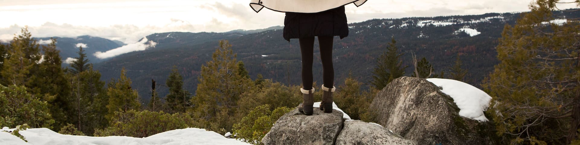 Young woman standing on rock on snow covered mountain, rear view, Twain Harte, California, USA