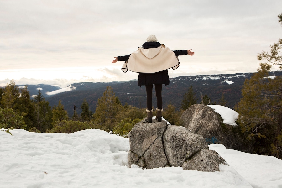 Young woman standing on rock on snow covered mountain, rear view, Twain Harte, California, USA
