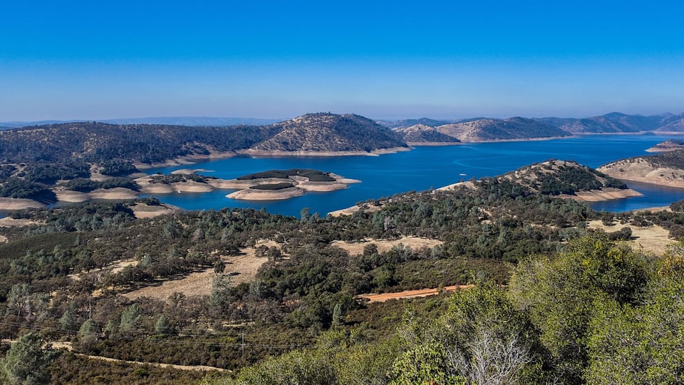 A coastal landscape with a large body of water, surrounded by hills and dense forests.