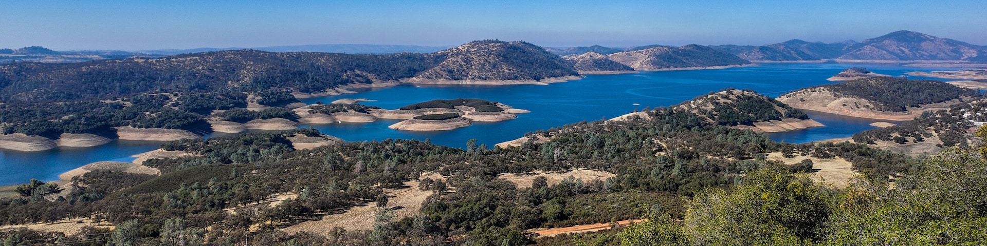 Paisagem costeira com uma grande massa de água, rodeada por colinas e florestas densas.