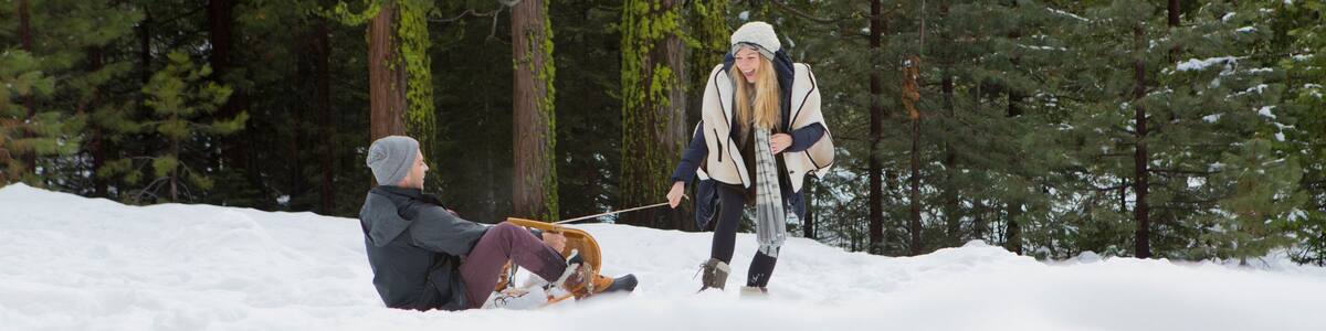 Young woman pulling boyfriend on sledge in winter forest, Twain Harte, California, USA