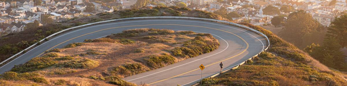 A winding road curving through a hilly landscape with a town in the background.