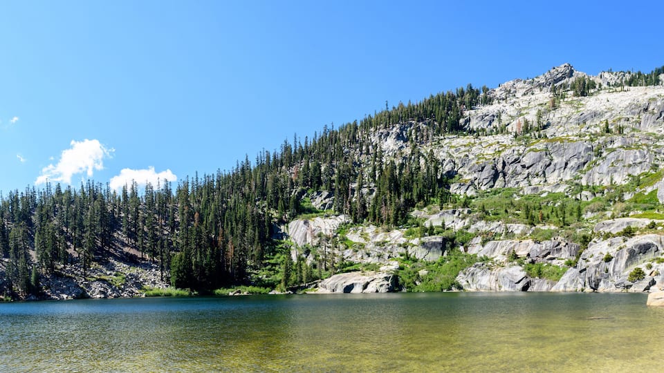 A clear lake surrounded by rocky mountains and dense forests.