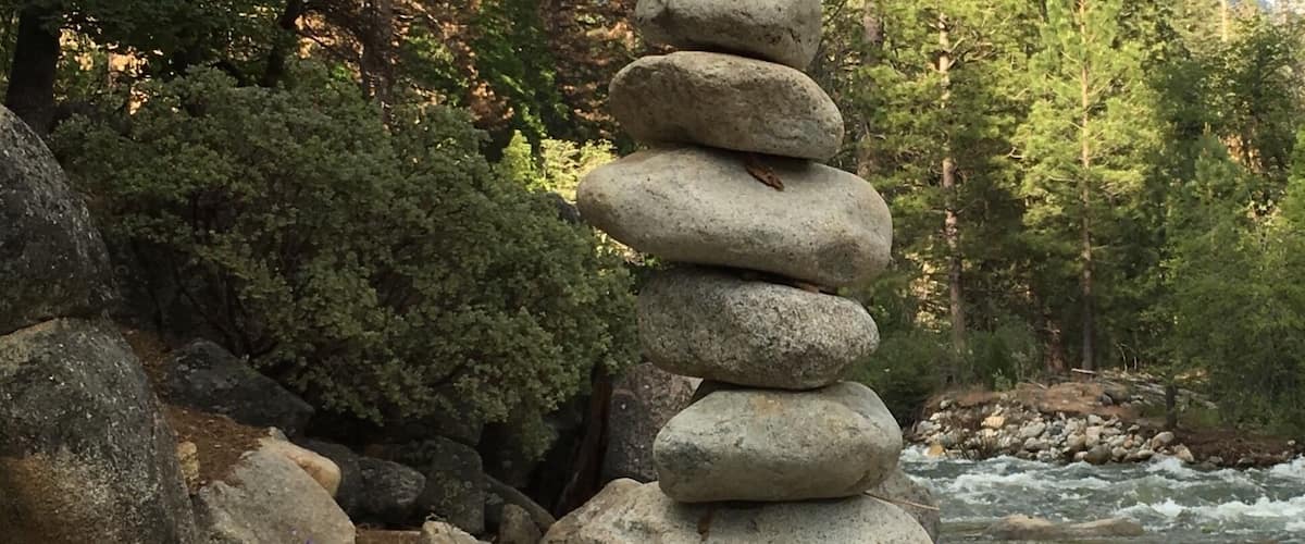 A stack of stones in a forested area with a river in the background.