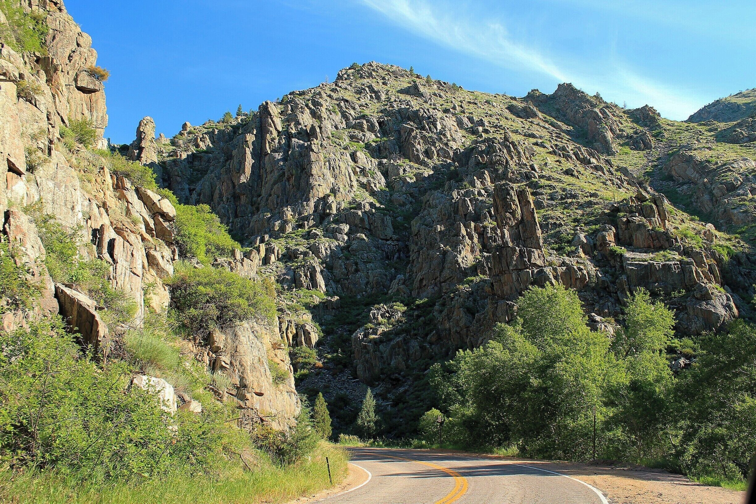 A winding mountain road flanked by rocky cliffs and green vegetation.