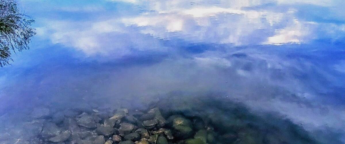 A calm lake with clear water reflecting a mountainous landscape.