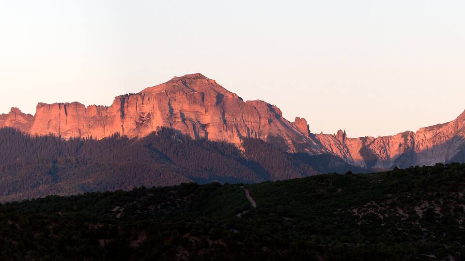 A mountain range with rugged peaks and a forested foreground.