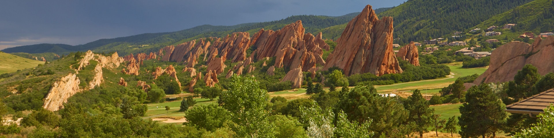 A landscape with red rock formations, green trees, and a golf course.