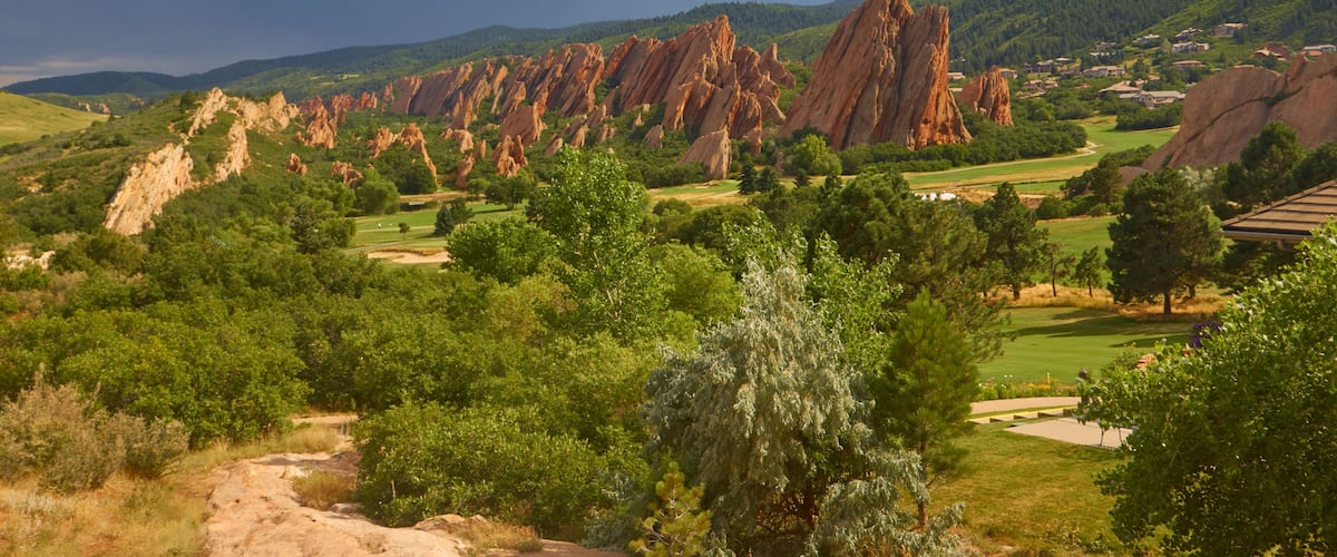 A landscape with red rock formations, green trees, and a golf course.