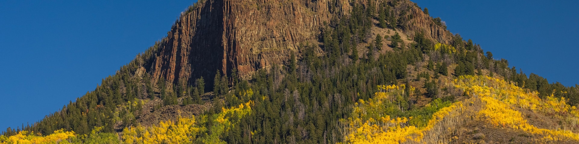 A mountain with a prominent peak, surrounded by yellow autumn foliage and dense forest.