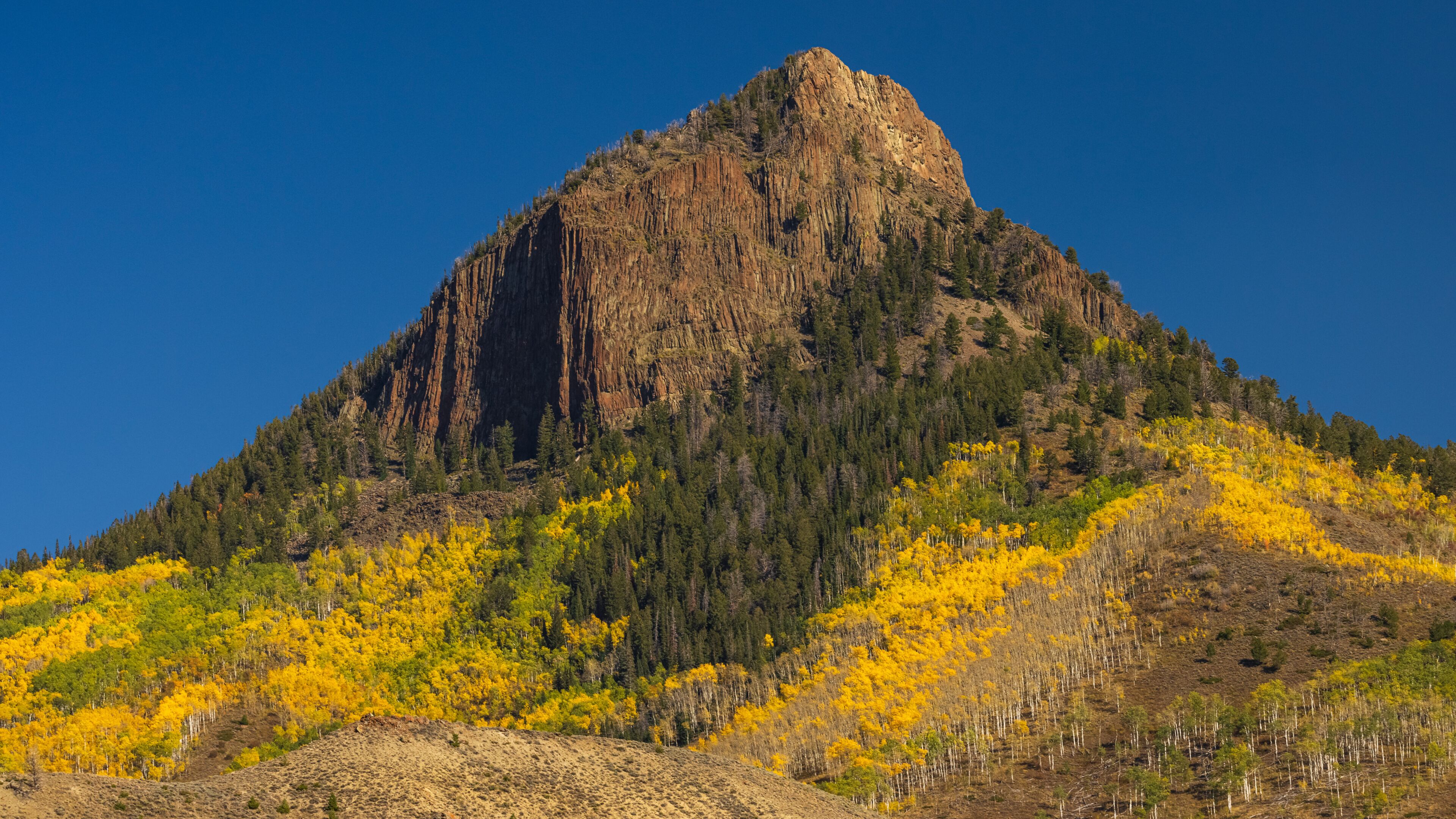 A mountain with a prominent peak, surrounded by yellow autumn foliage and dense forest.