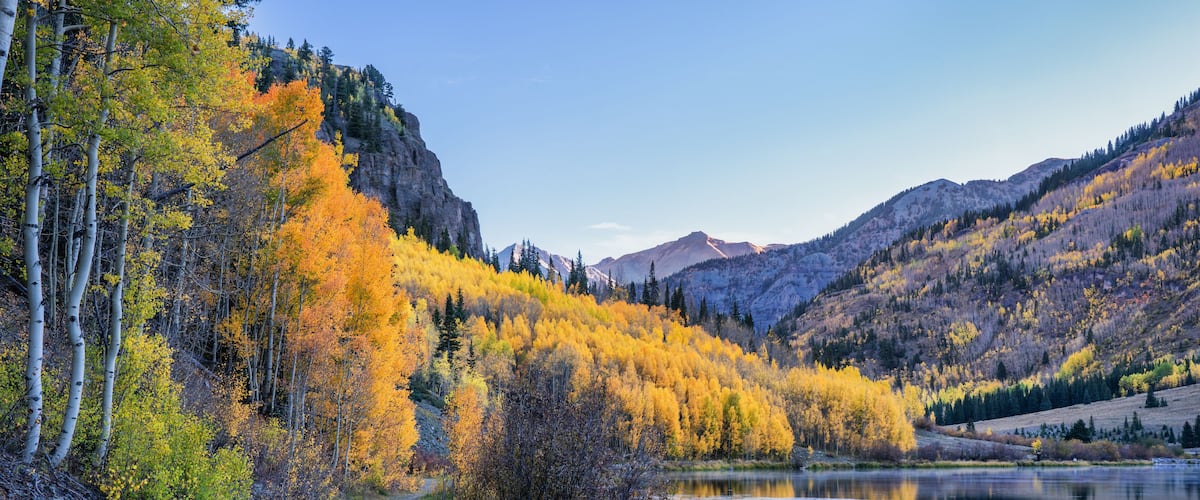 A mountain landscape with autumn foliage, a lake, and a clear sky.