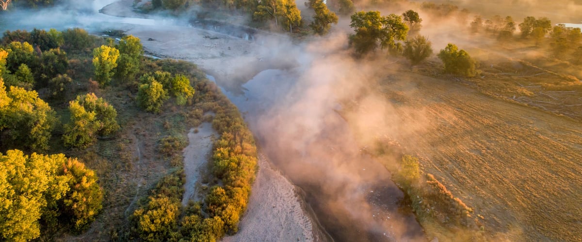 A river winding through a forested landscape with mist rising from the water.