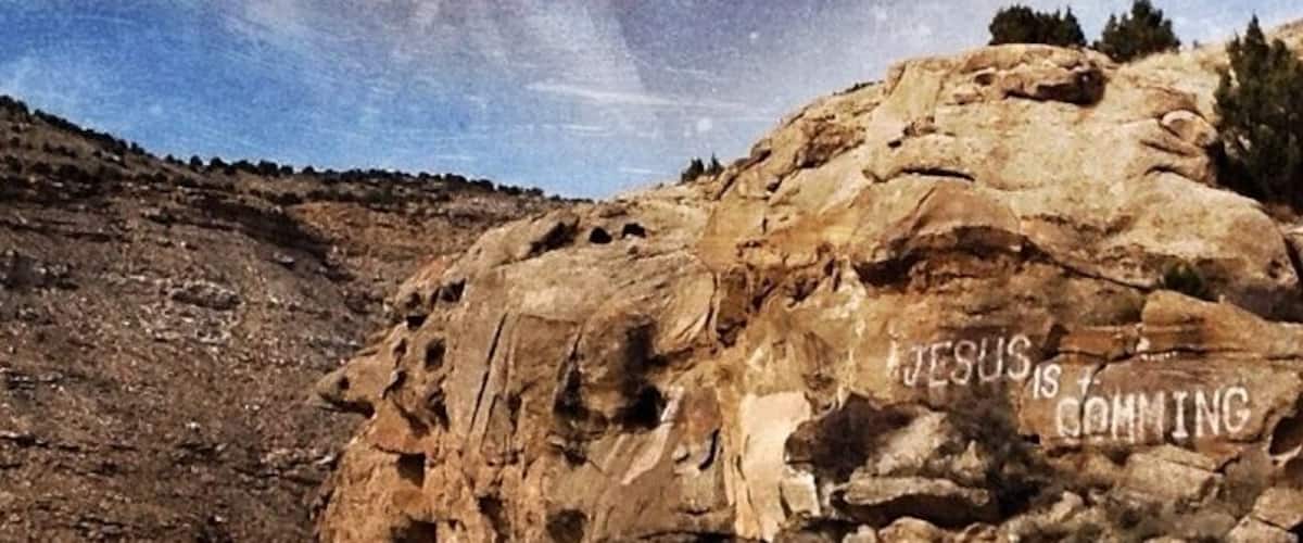 A winding road with a rocky cliff and the text "JESUS IS COMING" on it.