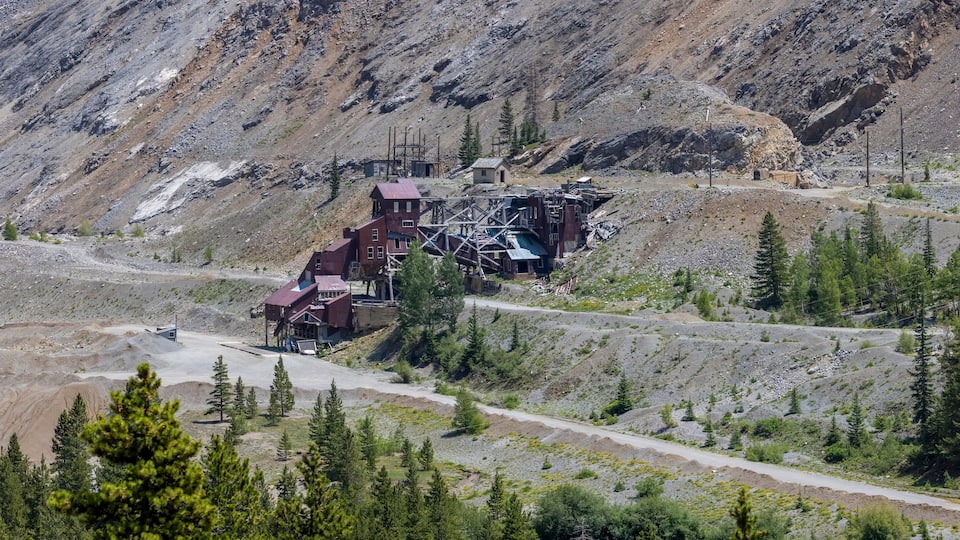 A mountainous landscape with a damaged building structure surrounded by trees and a winding road.