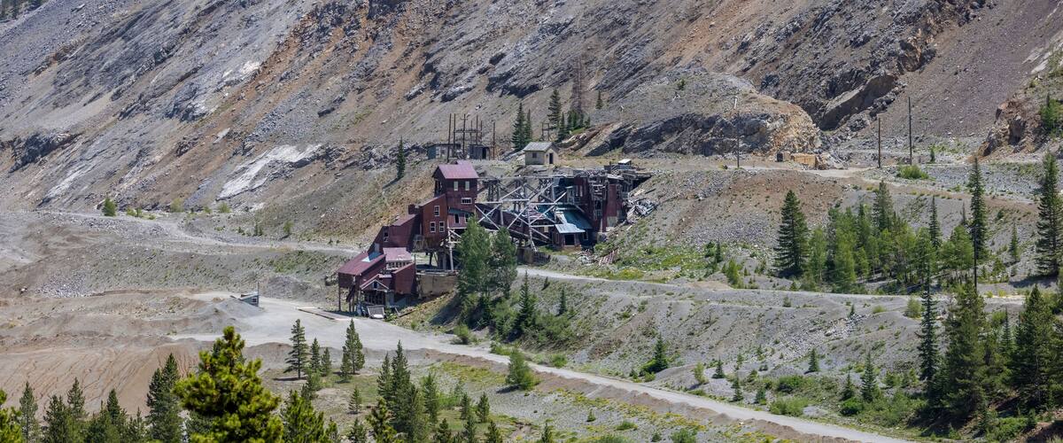 A mountainous landscape with a damaged building structure surrounded by trees and a winding road.