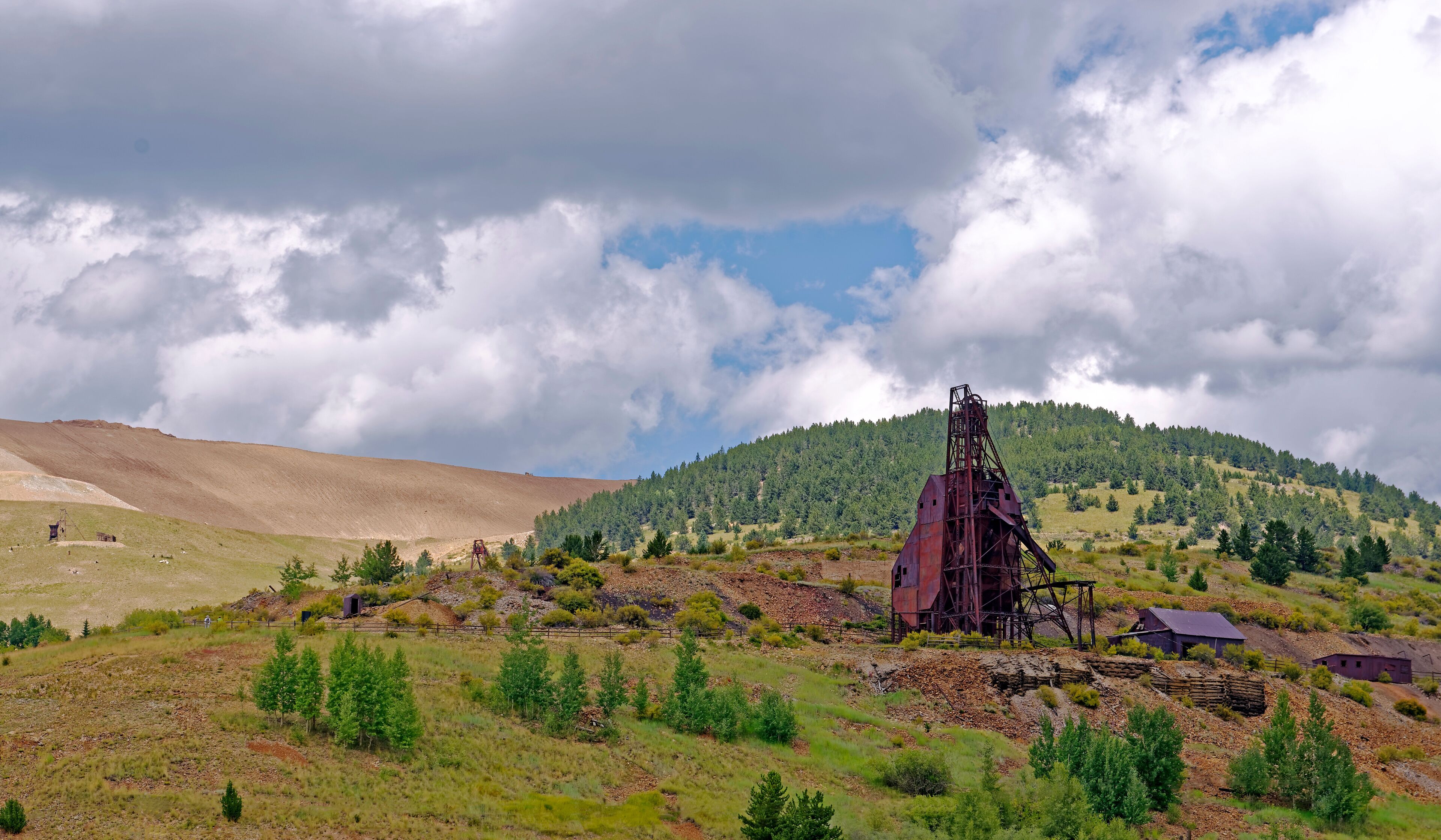 Equipment remains of 19th Century deep gold mining operations near Victor, Colorado, U.S.A. with spoil from the current Cripple Creek Mining District open cast gold mine in the background