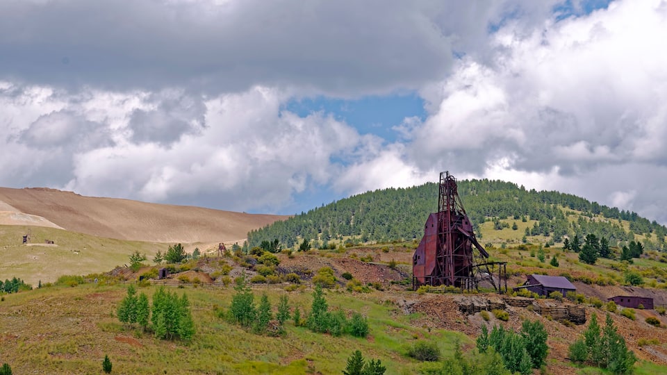 A mining site with a large red structure, a fenced area with trees, and a hill with dense forest in the background.