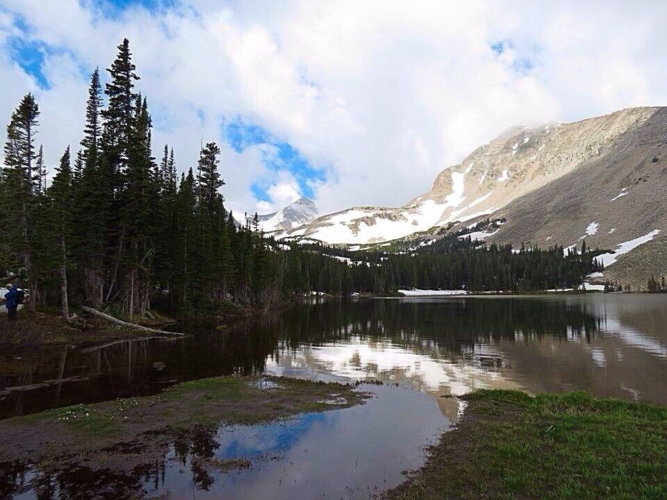 A mountain lake surrounded by evergreen trees and snow-capped peaks.