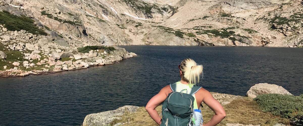 A person with a backpack overlooking a lake surrounded by rocky mountains.