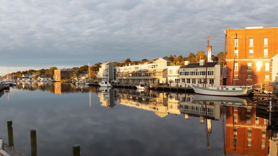 A calm river with boats, wooden docks, and buildings along the shore.