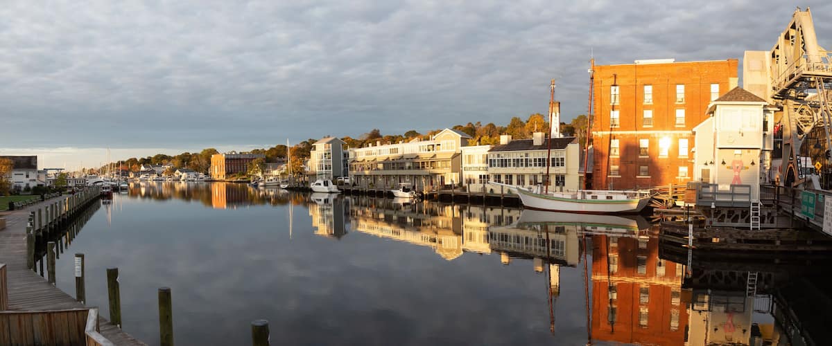 A calm river with boats, wooden docks, and buildings along the shore.