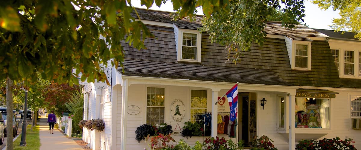 A quaint white building with a dark shingled roof, a flag, and a sign reading "Toys Ahoy".