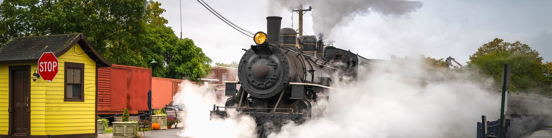 Retro-style historical steam train in motion on the train track in Essex, Connecticut. White steam clouds encircling and rising over the train.